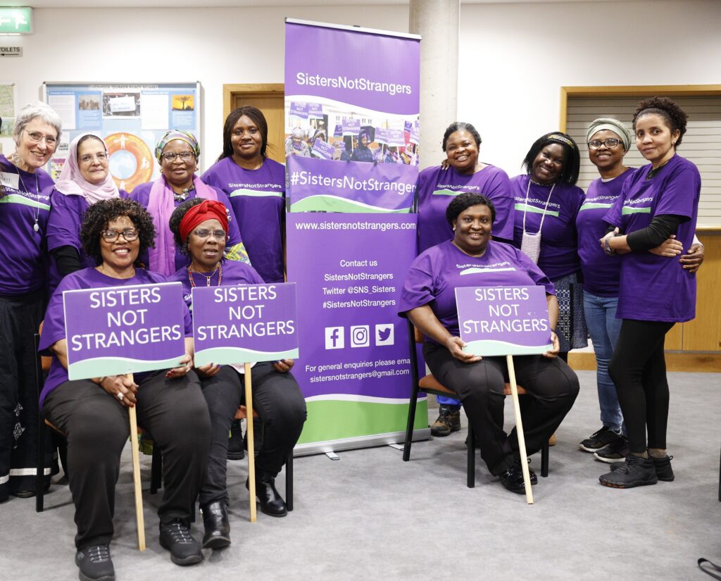 Sisters Not Strangers coalition members indoors wearing purple campaign t-shirts and holding placards